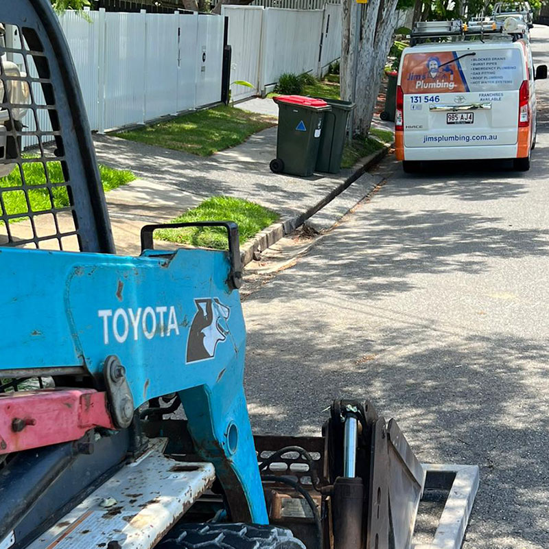 Excavator on street with Jim's Plumbing van in background