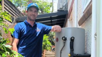 Plumber standing next to outdoor storge tank gas hot water system