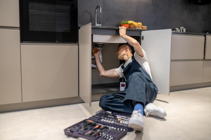 Man under kitchen sink plumbing