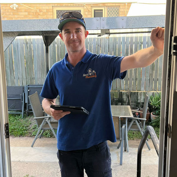 Plumber smiling in front of hot water system outside